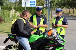 Na obrazie widać policjanta i policjantkę, którzy wykonują czynności z motocyklistą